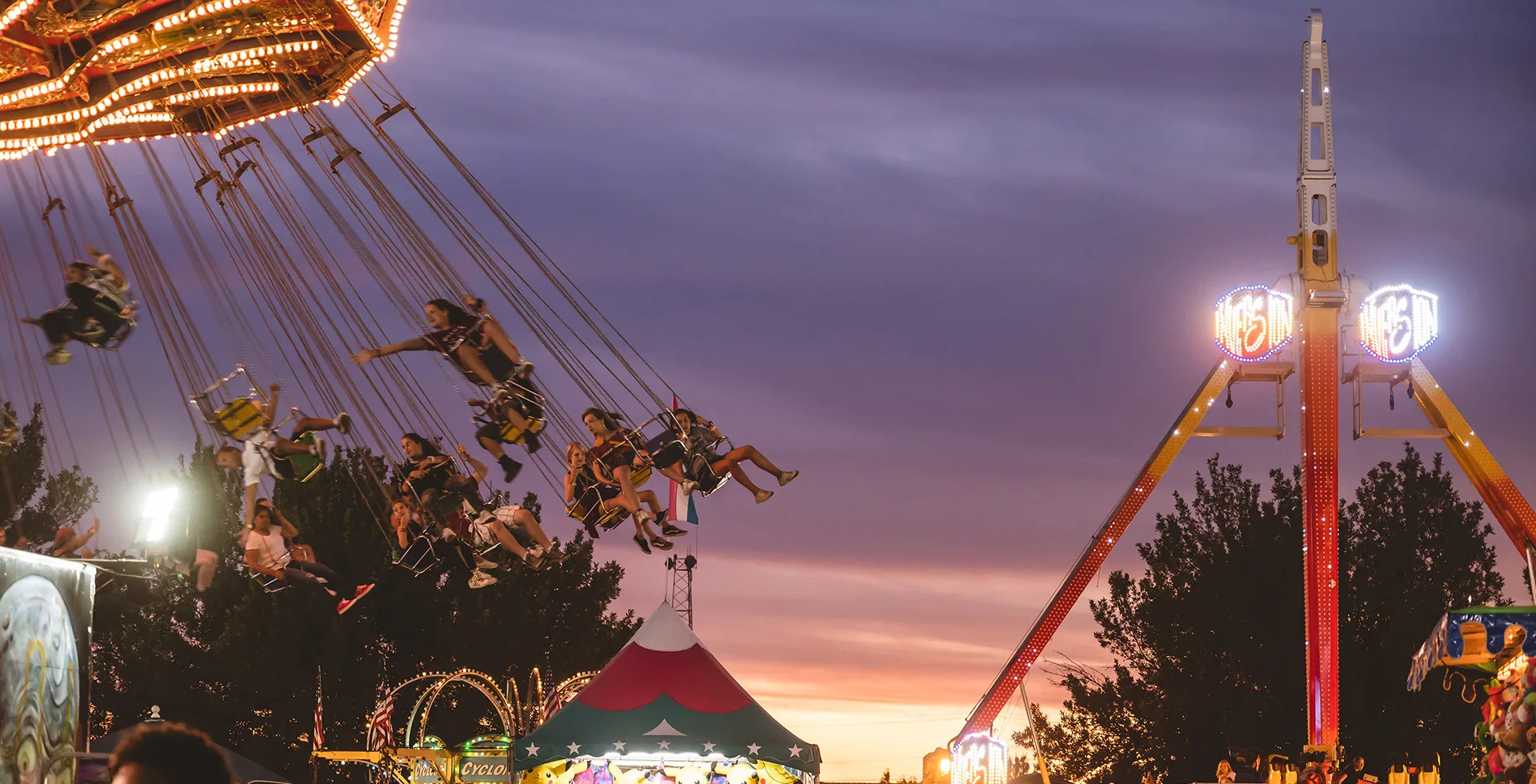 Fair-goers enjoy carnival rides as the sun sets.